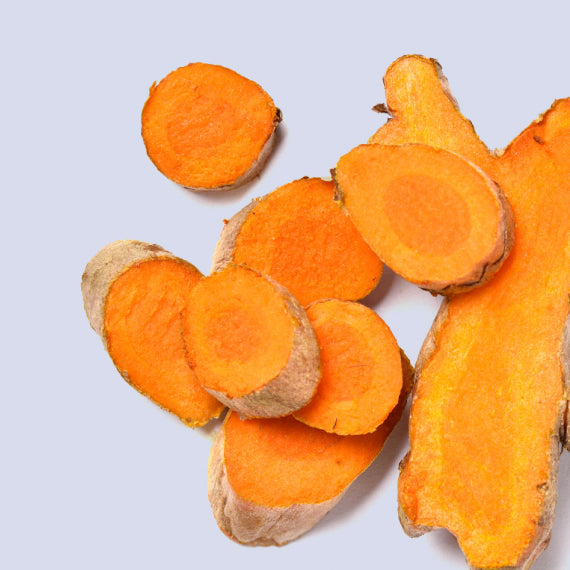Close-up of thin slices of curcumin root placed on a table. The slices are golden-yellow in color with a slightly rough texture. Curcumin is a PCOS supplement known for its anti-inflammatory properties and its potential to help manage PCOS symptoms by supporting hormonal balance and improving insulin sensitivity.