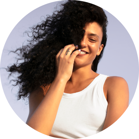 Smiling woman in a white tank top holding back her curly hair